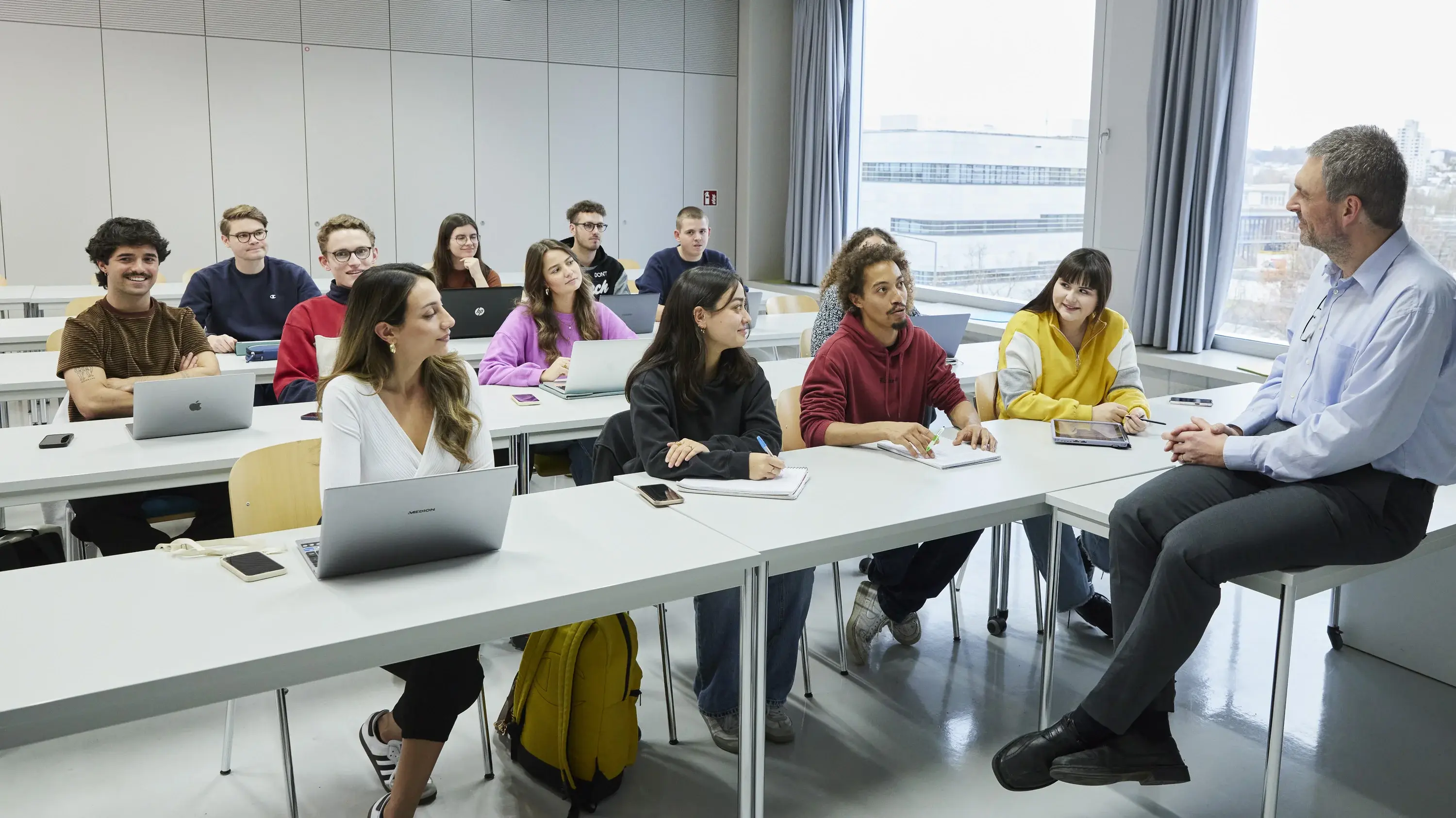 Professor sitzt auf seinem Tisch vor Studierenden in der Vorlesung.