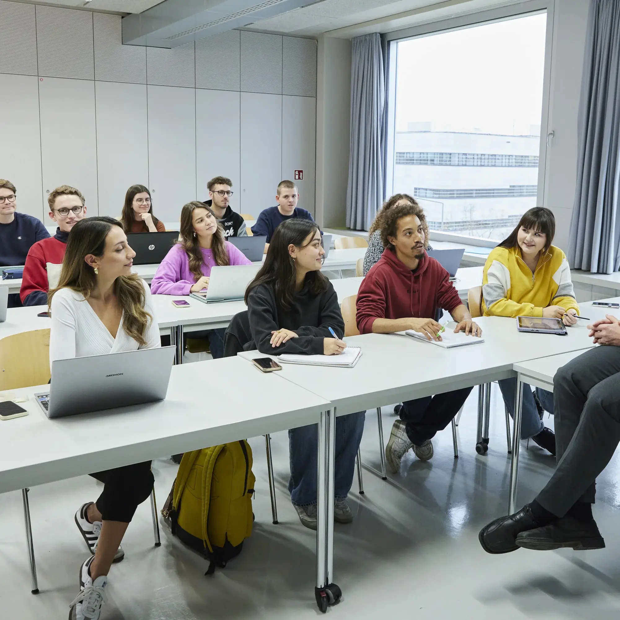 Professor sitzt auf seinem Tisch vor Studierenden in der Vorlesung.