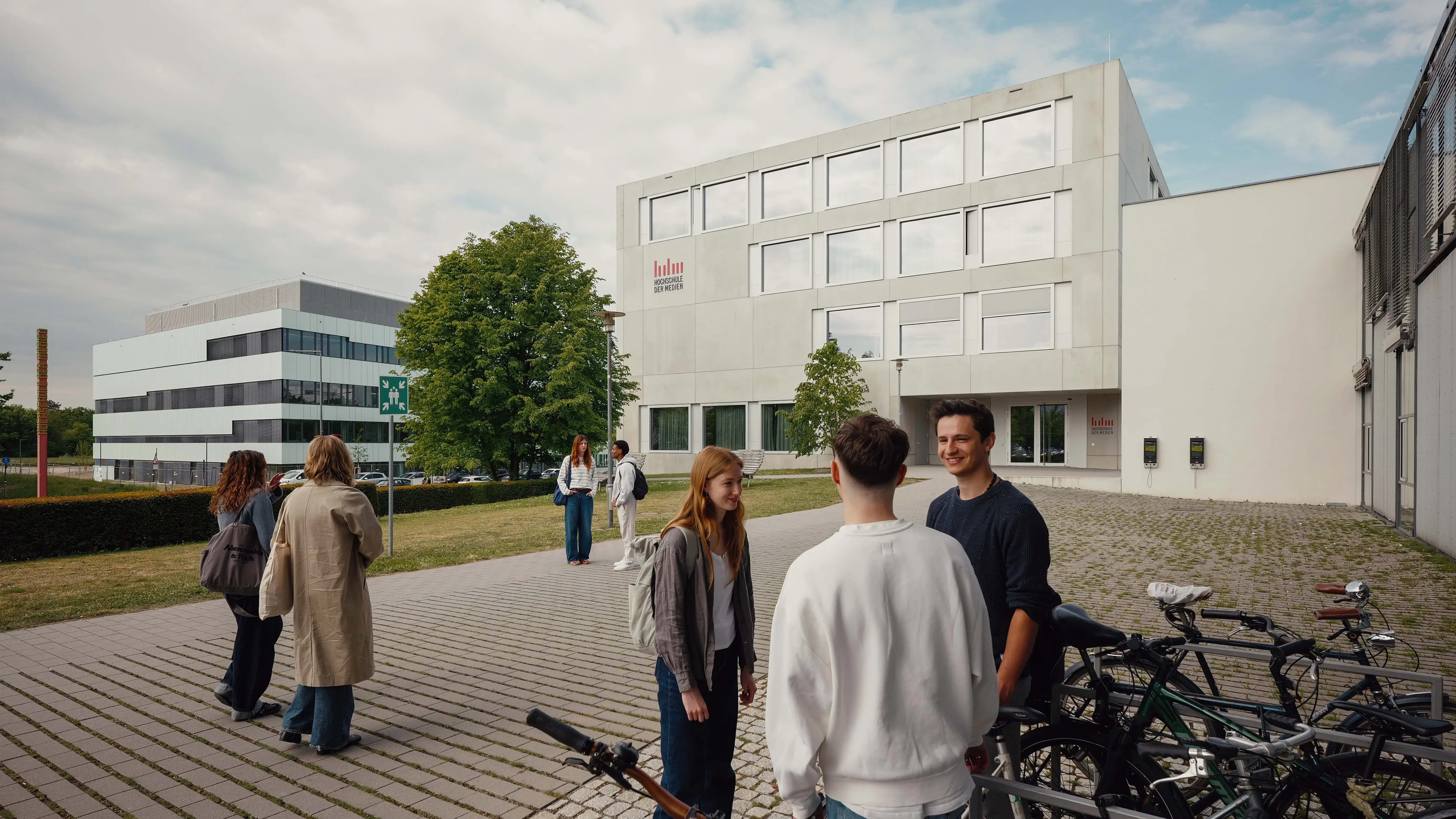 Studierende unterhalten sich bei den Fahrradständern vor einem Nebengebäude der Hochschule der Medien.